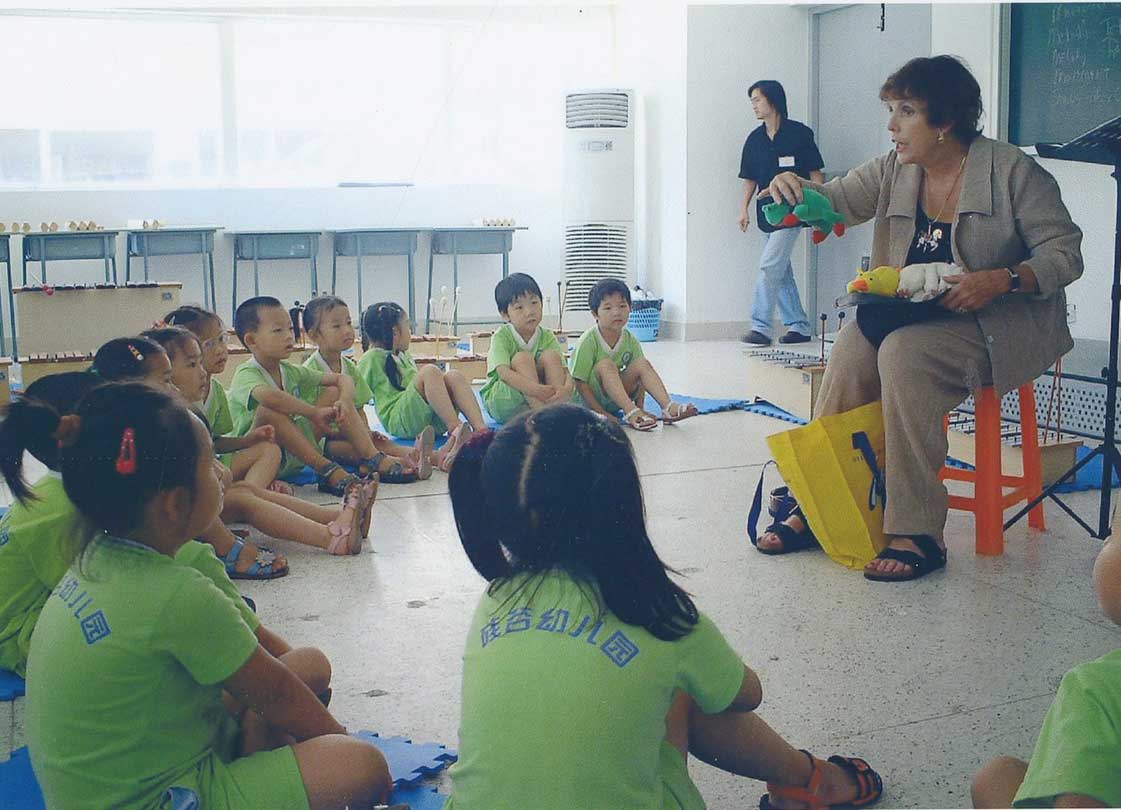 Teacher sits amongst a group of school children holding stuffed animals.