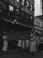Women marching in a suffrage parade carrying banner, "Preparedness" in front of Rhodes Jennings furniture store.