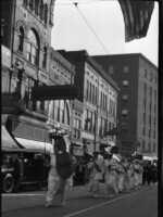 Women marching in parade, one carrying spear & shield marked, "Victory".